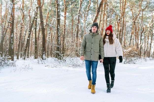 若い白人カップルが雪に覆われた森を歩いています。