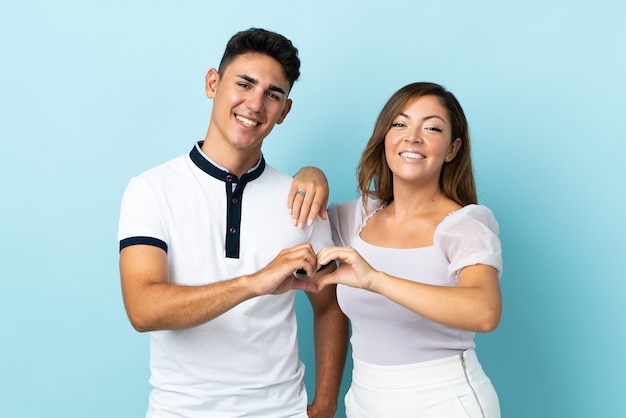 Young caucasian couple on blue making a heart with hands