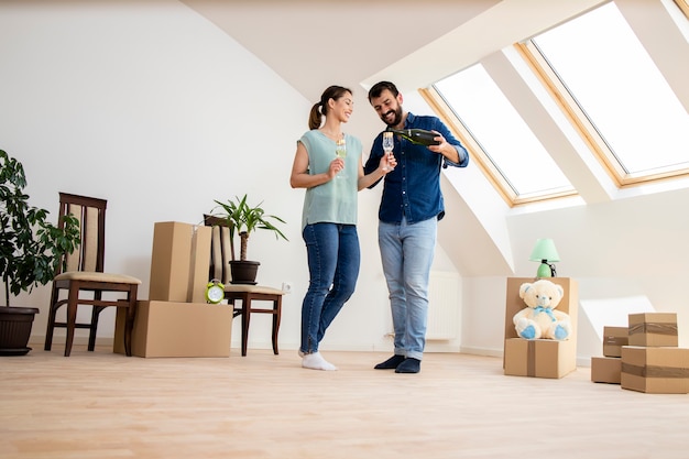 Young caucasian couple dancing and drinking champagne to celebrate moving into new home.