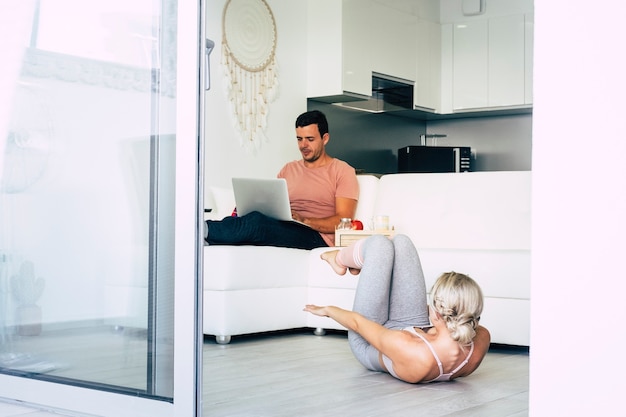 Young caucasian couple inside beautiful home work at laptop computer and do exercise fitness lifestyle