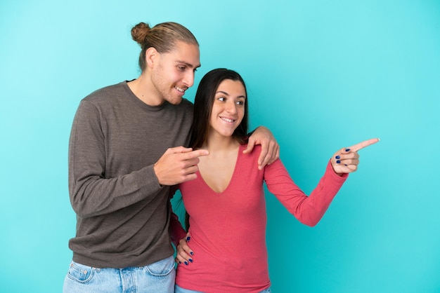 Young caucasian couple isolated on blue background pointing finger to the side