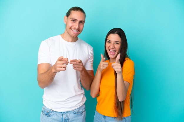 Young caucasian couple isolated on blue background points finger at you