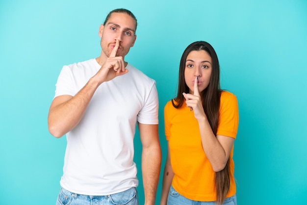 Young caucasian couple isolated on blue background showing a sign of closing mouth and silence gesture