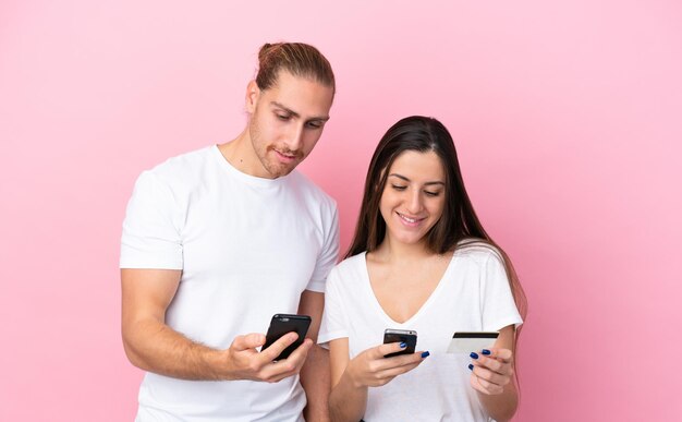 Молодая кавказская пара, изолированная на розовом фоне, покупает с помощью мобильного телефона с помощью кредитной карты