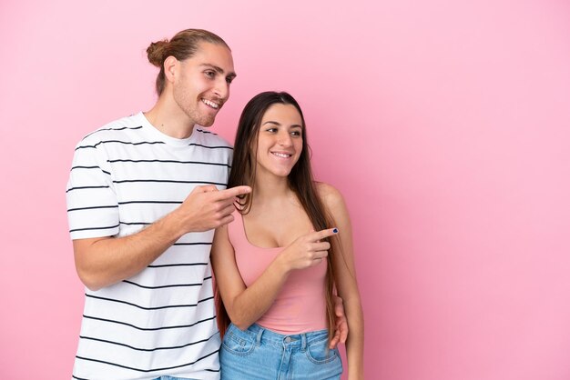 Young caucasian couple isolated on pink background pointing finger to the side