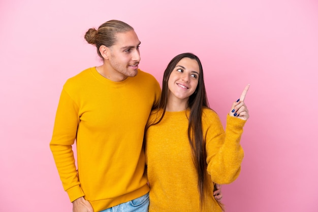 Young caucasian couple isolated on pink background pointing to the side to present a product