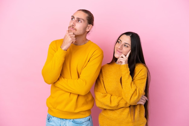 Young caucasian couple isolated on pink background thinking an idea while looking up