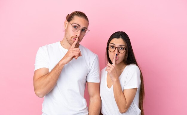 Young caucasian couple isolated on pink background With glasses and doing silence gesture