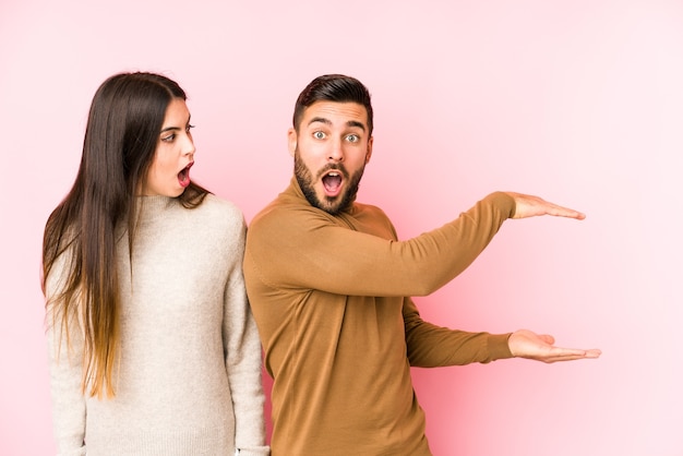 Photo young caucasian couple isolated shocked and amazed holding a copy space between hands.