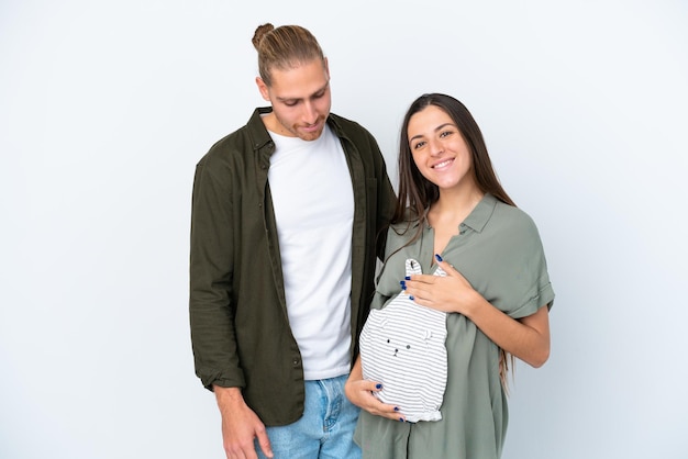 Young caucasian couple isolated on white background pregnant and holding baby clothes