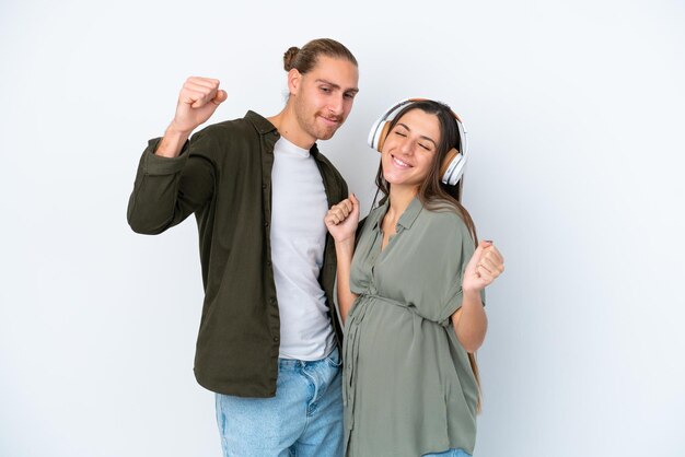 Young caucasian couple isolated on white background pregnant and listening music