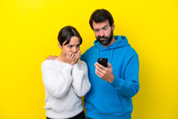 Молодая кавказская пара, изолированная на желтом фоне, читает сообщение с мобильного телефона