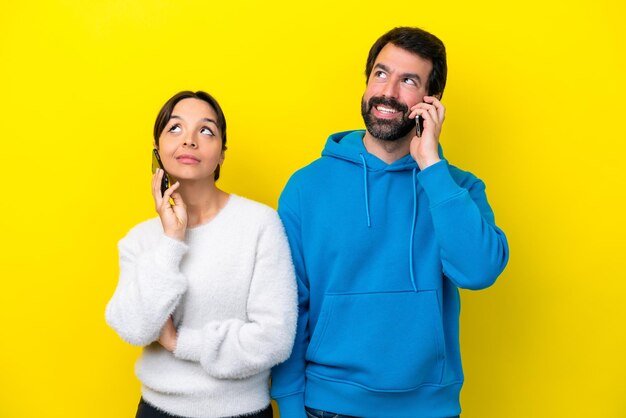 Young caucasian couple isolated on yellow background talking to mobile