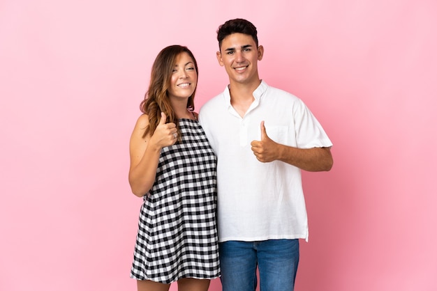 Young caucasian couple on pink giving thumbs up gesture