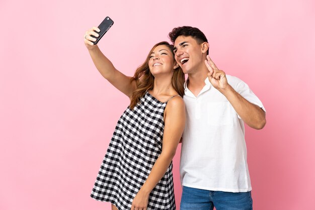 Young caucasian couple on pink making a selfie with the mobile