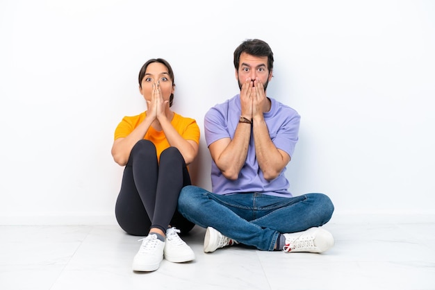 Young caucasian couple sitting on the floor isolated on white background with surprise facial expression