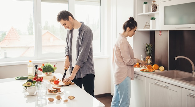 Giovani coppie caucasiche affettare frutta in cucina e preparare la colazione insieme