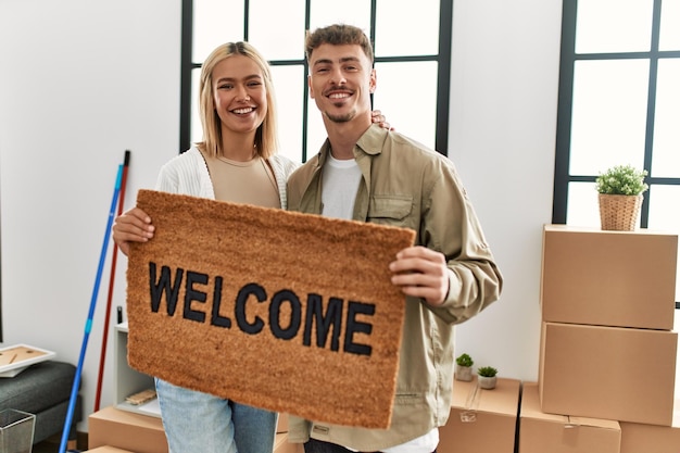 Young caucasian couple smiling happy holding welcome doormat at new home.
