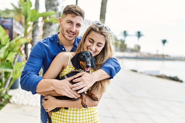 Young caucasian couple smiling happy and hugging with dog at the promenade.