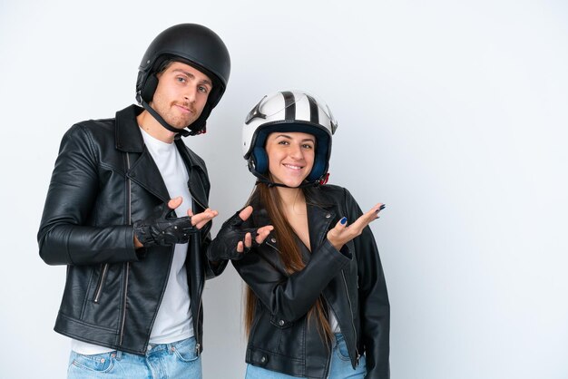 흰색 배경에 격리된 오토바이 헬멧을 쓴 백인 젊은 부부는 초대하기 위해 손을 옆으로 뻗었다