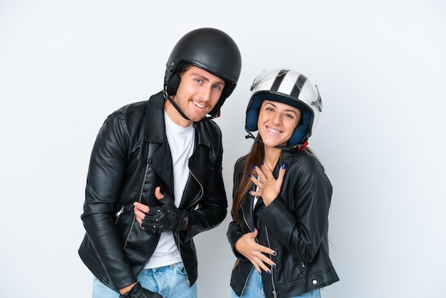 胸に手を置いている間たくさん笑っている白い背景で隔離のオートバイのヘルメットと若い白人カップル