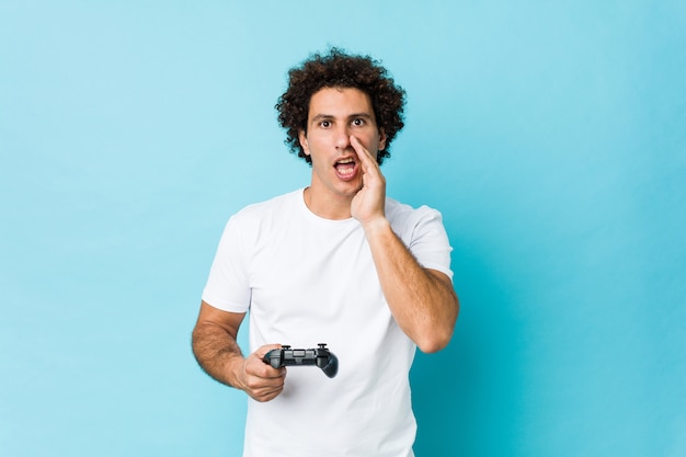 Young caucasian curly man holding a game controller shouting excited to front.