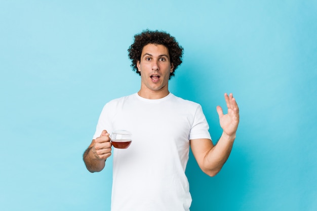 Young caucasian curly man holding a tea cup celebrating