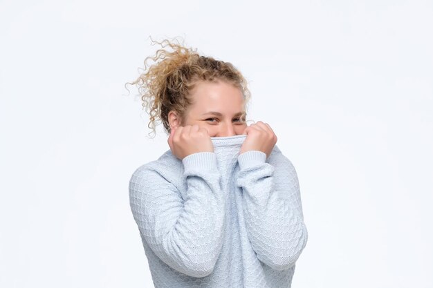 Photo young caucasian curly woman hiding face under blue sweater being shy