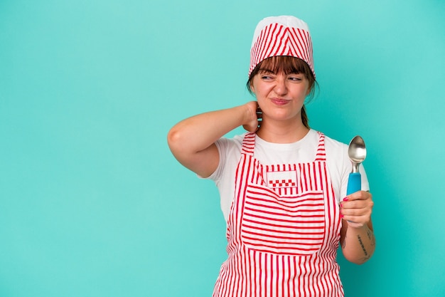 Young caucasian curvy ice cream maker holding a scoop isolated on blue background touching back of head, thinking and making a choice.