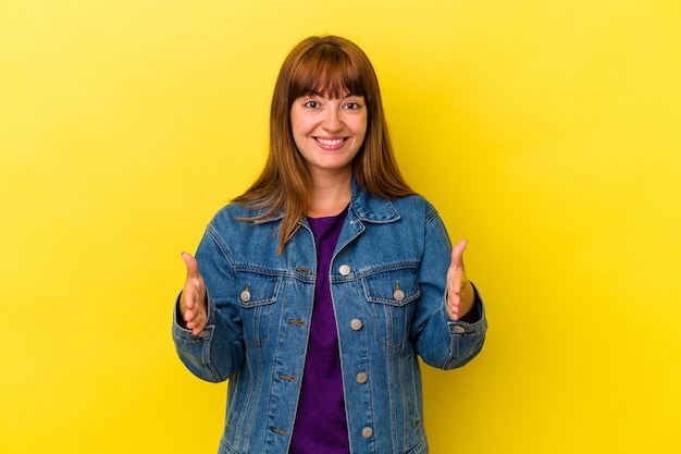 Young caucasian curvy woman isolated on yellow background holding something with both hands, product presentation.