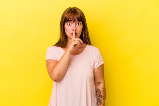 Young caucasian curvy woman isolated on yellow background keeping a secret or asking for silence.