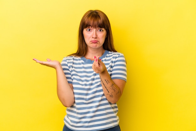 Giovane donna curvy caucasica isolata su fondo giallo che mostra che non ha soldi.