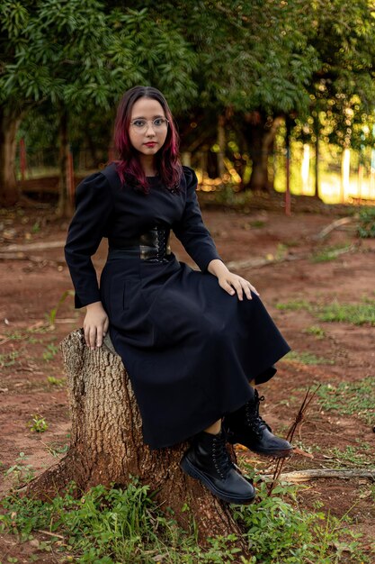 Young caucasian dark haired girl with red streaks in black dress outfit with corset belt and glasses posing for female beauty shoot