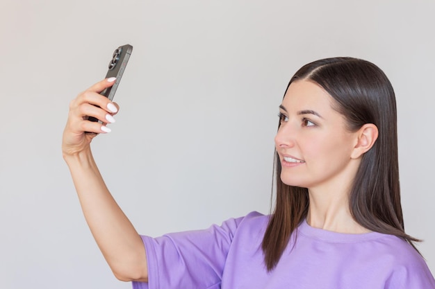 young Caucasian darkhaired pretty woman in a purple Tshirt takes a selfie on her phone and smiles