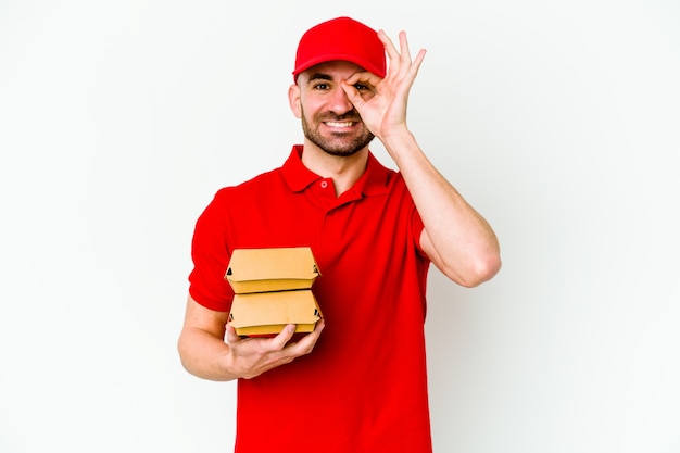 Young caucasian delivery man isolated on white wall excited keeping ok gesture on eye.