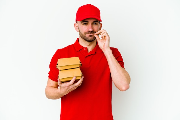 Young caucasian delivery man isolated on white wall with fingers on lips keeping a secret.