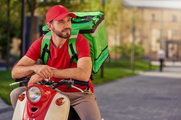 Photo young caucasian delivery man on scooter looking aside