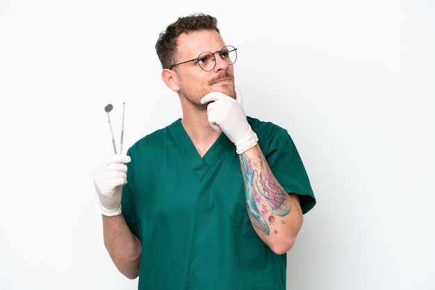 Young caucasian dentist man isolated on white background having doubts and thinking