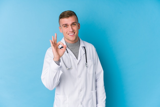 Young caucasian doctor man cheerful and confident showing ok gesture.