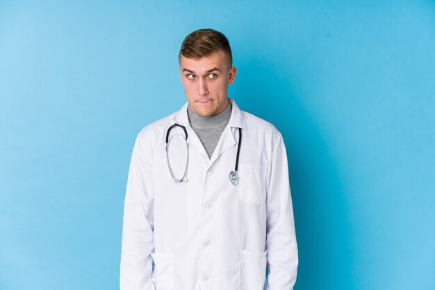 Young caucasian doctor man confused, feels doubtful and unsure