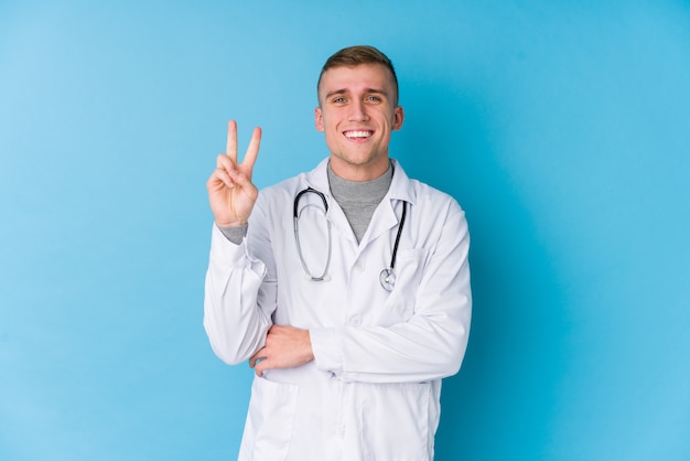 Young caucasian doctor man showing number two with fingers.