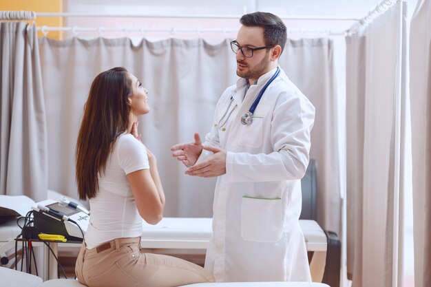 Young Caucasian doctor in white uniform examining patient's throat while standing at hospital.