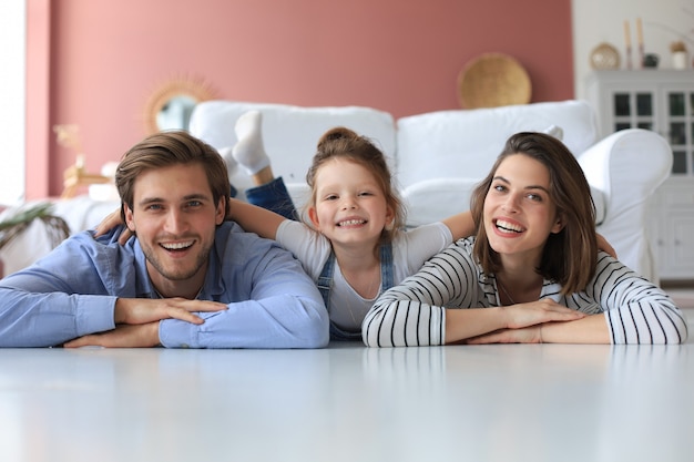 Young Caucasian family with small daughter pose relax on floor in living room, smiling little girl kid hug embrace parents, show love and gratitude, rest at home together.