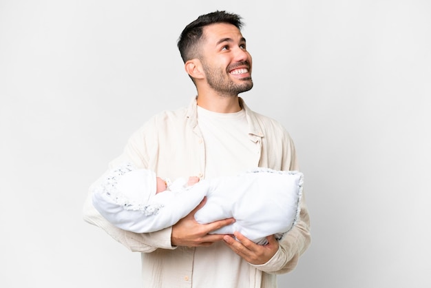 Young caucasian father with her newborn baby over isolated background looking up while smiling