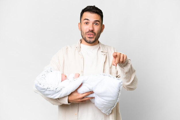 Молодой кавказский отец с новорожденным ребенком на изолированном фоне удивлен и указывает вперед