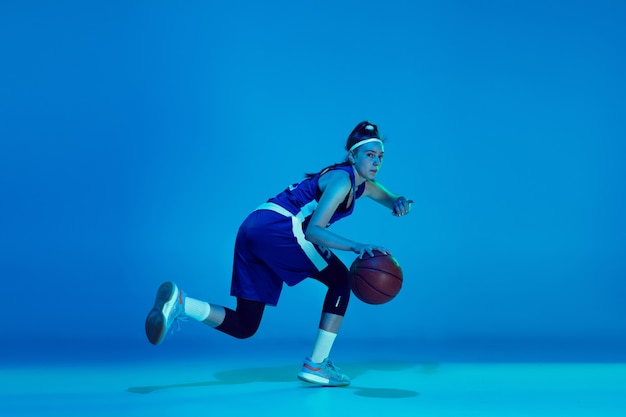 Young caucasian female basketball player isolated on blue\
studio background in neon light