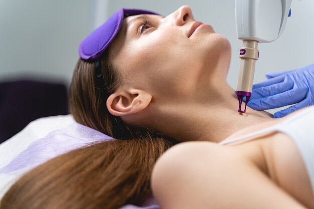 Young Caucasian female patient undergoing a laser mole removal procedure in a professional beauty clinic