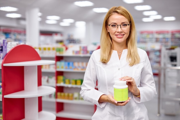 Young caucasian female pharmacist is showing medicine box