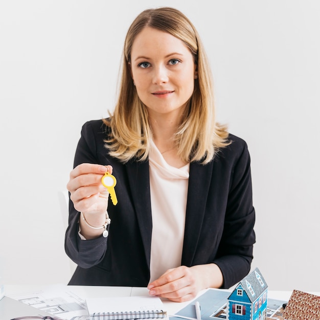 Young caucasian female real estate agent holding key looking at camera