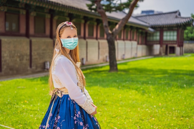 Молодая кавказская туристка в медицинской маске в национальном корейском платье ханбок путешествует по корее